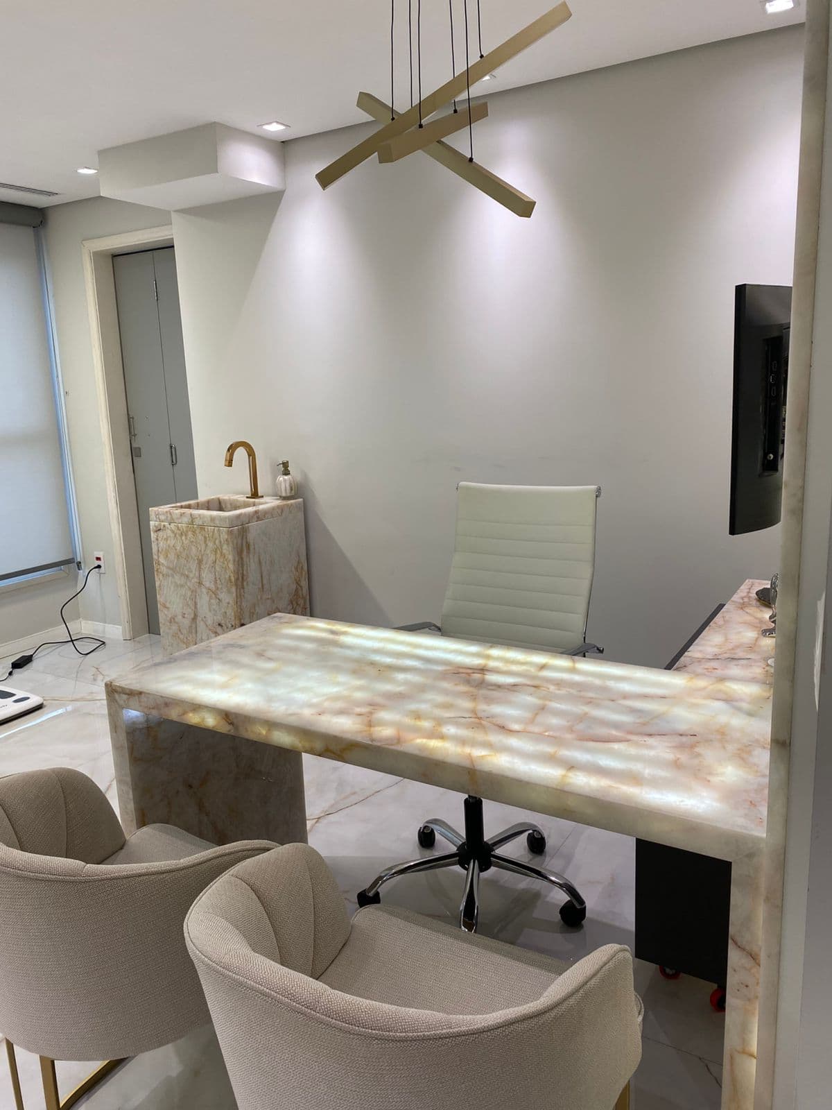 Mesa de consulta de endocrinologia da Dra. Débora Di Matteo, com cadeira branca e luminária pendente, no consultório no Jardins, São Paulo