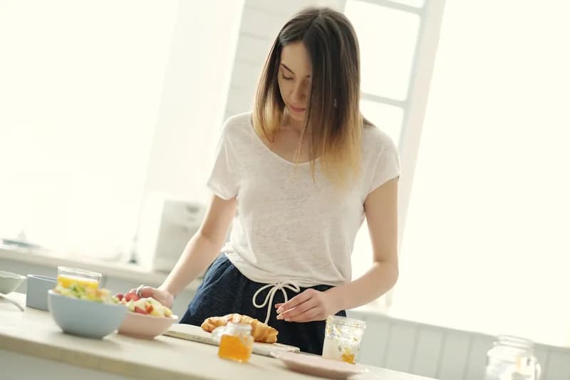 Mulher preparando o café da manhã na cozinha, ilustrando conteúdo sobre alimentação e glicemia.