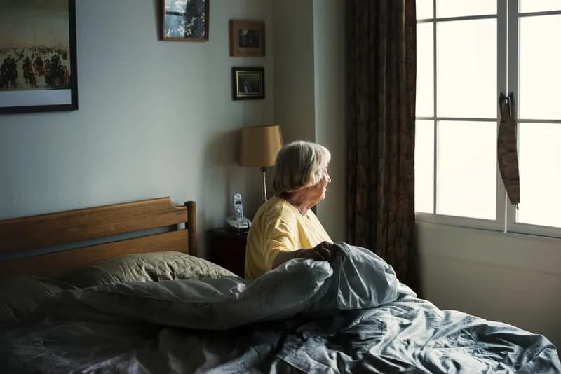 Mulher madura sentada na cama olhando pela janela, ilustrando conteúdo sobre insônia na menopausa.