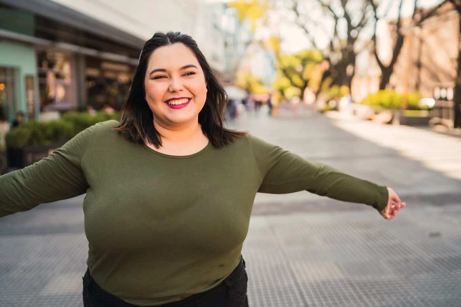 Mulher sorrindo de braços abertos em ambiente urbano, ilustrando conteúdo sobre obesidade não ser falta de esforço.