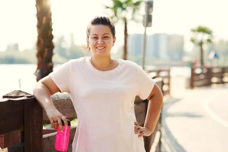 Mulher sorrindo numa pausa do exercício ao ar livre, à beira d'água
